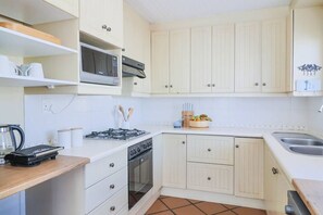 Une cuisine de taille réduite avec des meubles blancs, une cuisinière à gaz, un four à micro-ondes et un évier.