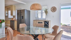 A modern kitchen with a refrigerator, a dining table with chairs, and a hanging light fixture.