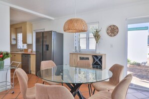 A modern kitchen with a refrigerator, a dining table with chairs, and a hanging light fixture.