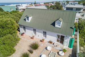 A single-story house with a green roof, a small attached garage, and a paved driveway with potted plants.