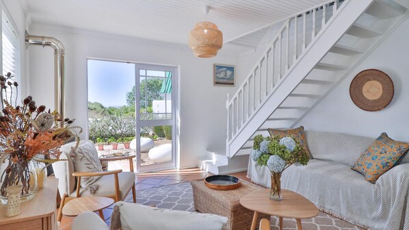 Un amplio salón con una escalera, una mesa de comedor y un sofá con cojines decorativos.