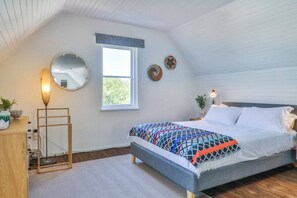 Une chambre à coucher comprenant un lit, une table de chevet, une lampe, un miroir, une fenêtre et des éléments décoratifs sur le mur.