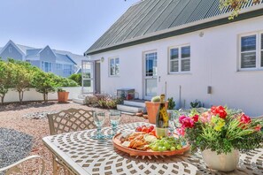 An outdoor dining area with a table set for a meal, a bottle of wine, and a variety of fruits and vegetables.