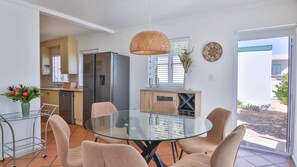 Una cocina moderna con refrigerador, una mesa de comedor con sillas, una lámpara colgante y vistas al exterior.