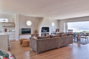 Una sala de estar moderna con un sofá grande, un televisor de pantalla plana y un comedor con vista al océano.