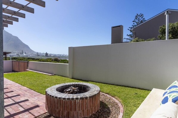 A patio with a fire pit, a grassy area, and a view of a cityscape.