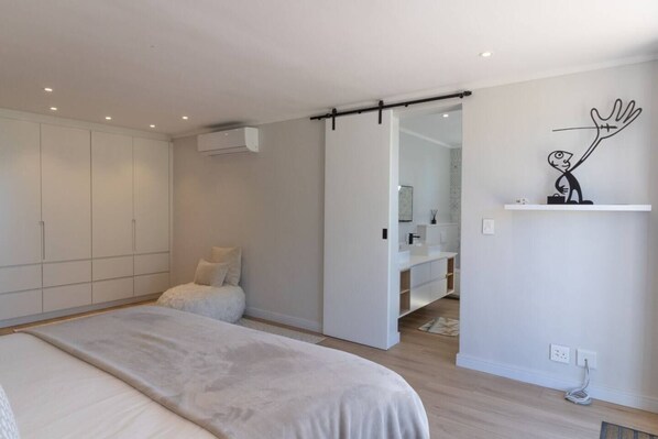 A bedroom with a bed, a wardrobe, a sliding door leading to a bathroom, and a minimalist wall art piece.