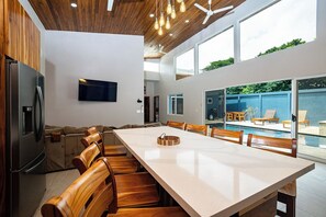 Eine moderne Küche mit einer großen Kochinsel, Holzkstühlen, einem eingebauten Backofen und einem an der Wand befestigten Fernseher.