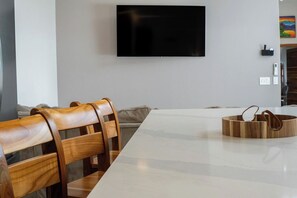 Ein zeitgenössischer Essbereich mit einem langen Tisch, Holzstühlen und einem an der Wand befestigten Flachbildfernseher.