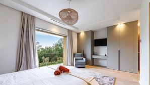Une chambre à coucher moderne avec un grand lit, une vue sur la verdure, un fauteuil gris et une armoire.