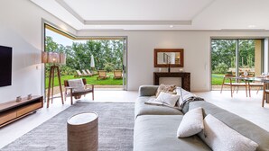Un salon moderne avec un grand canapé gris, une table basse et un téléviseur. On y trouve un meuble TV en bois et une grande fenêtre donnant sur l’extérieur.