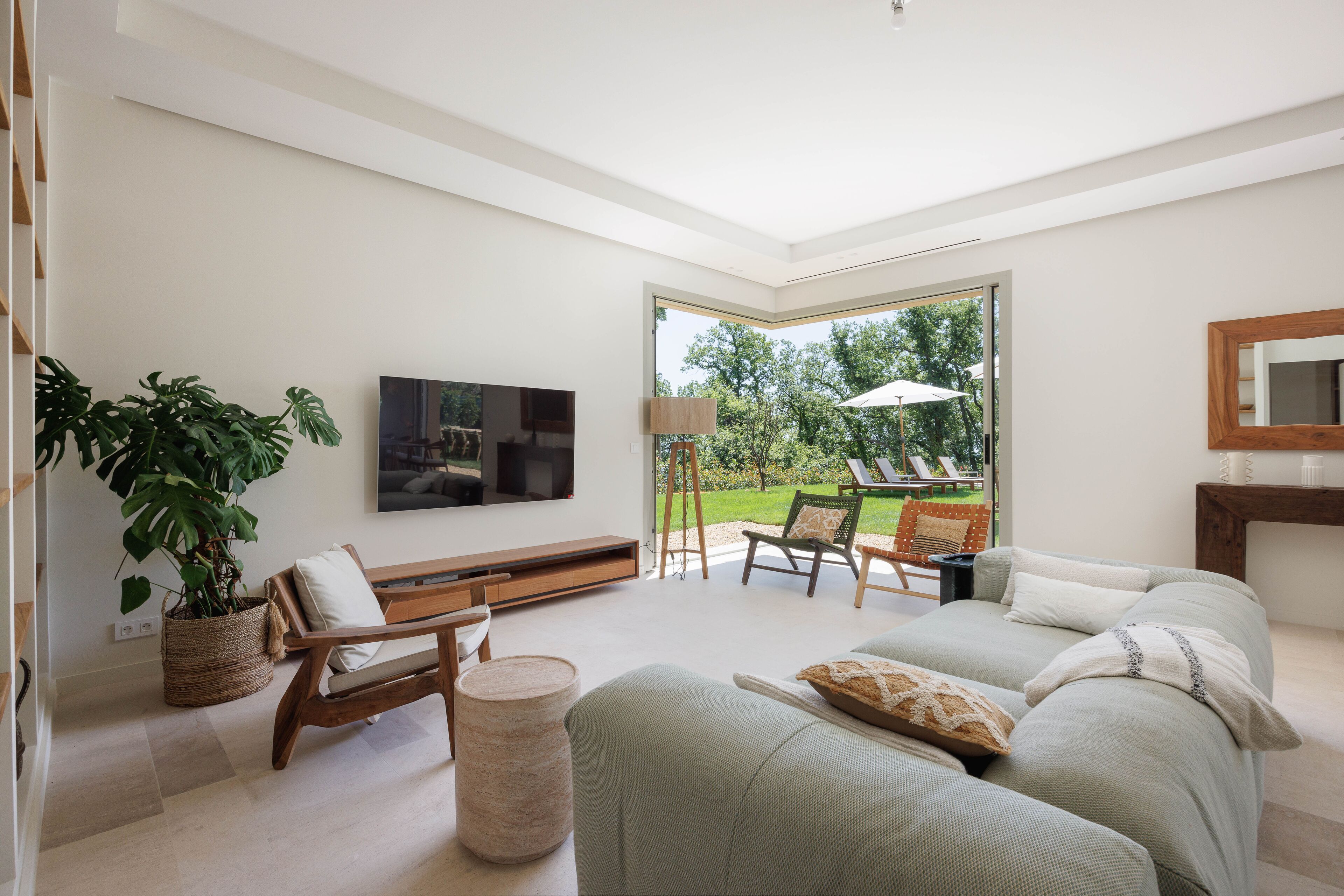 A modern living room with a sofa, chairs, a TV, and a large window overlooking a garden.