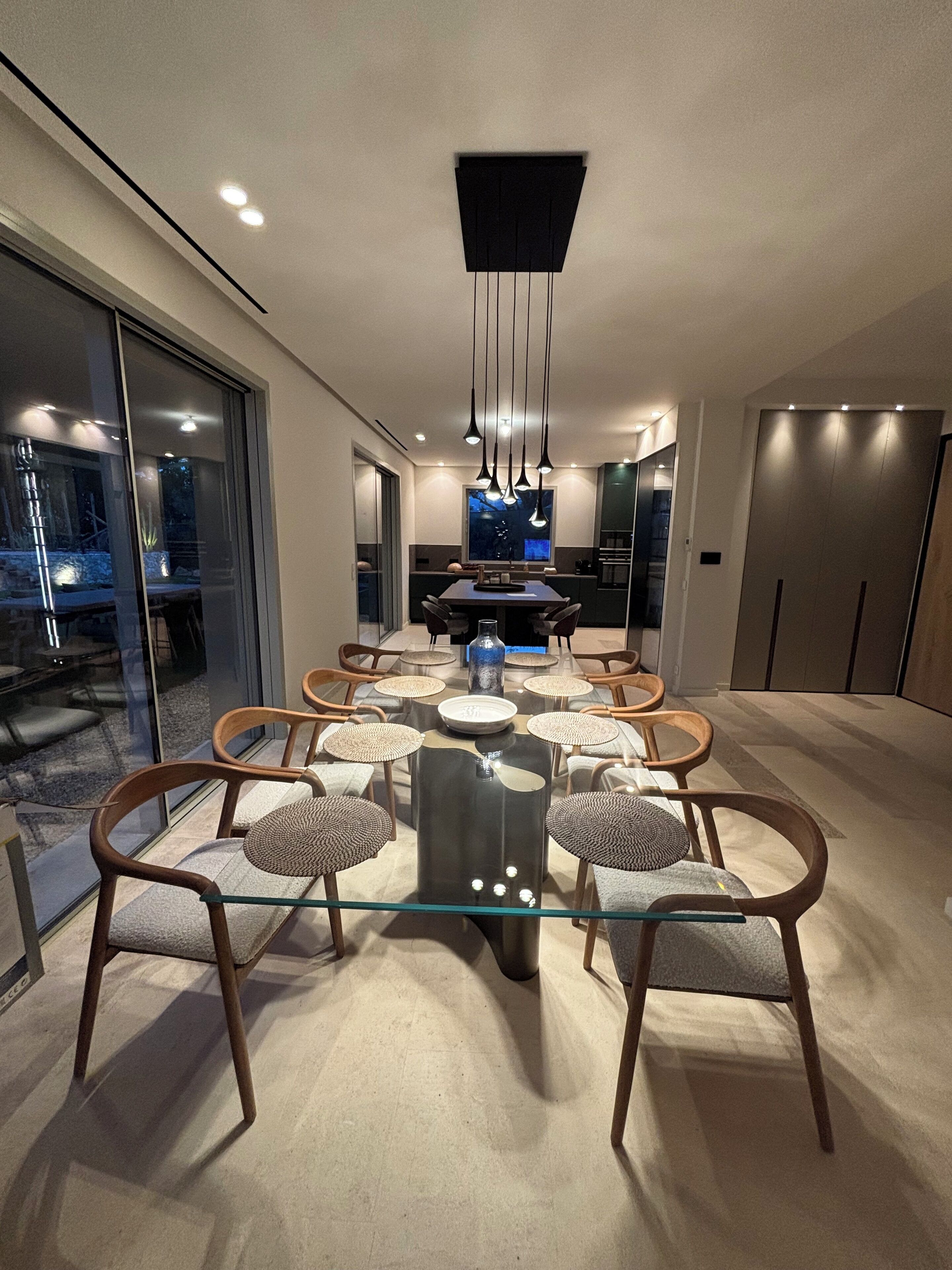 A modern dining area with a glass table, wooden chairs, and a central light fixture.