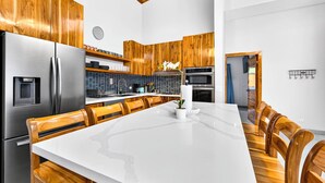Une cuisine moderne avec des meubles en bois, un réfrigérateur en acier inoxydable, un grand îlot central avec des sièges et un dosseret de carrelage bleu.