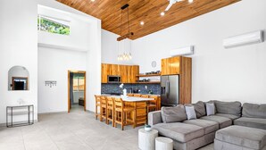 Un vaste espace de vie comprenant un grand canapé d’angle, un plafond en bois et une cuisine avec des meubles en bois.