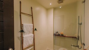 A modern bathroom with a glass shower enclosure, a wooden ladder with a towel, and a small shelf with toiletries. - UNLTD Hotel Siargao (General Luna)
