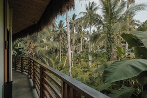 A wooden balcony with a thatched roof overlooking a lush tropical garden with tall palm trees. - UNLTD Hotel Siargao (General Luna)
