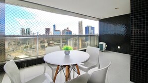 Ein modernes Zimmer mit rundem Tisch und weißen Stühlen, einer Topfpflanze und Blick auf die Stadt durch große Fenster.