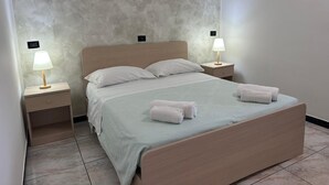 A neatly made bed with two pillows, two bedside lamps, and two rolled towels on the bed.