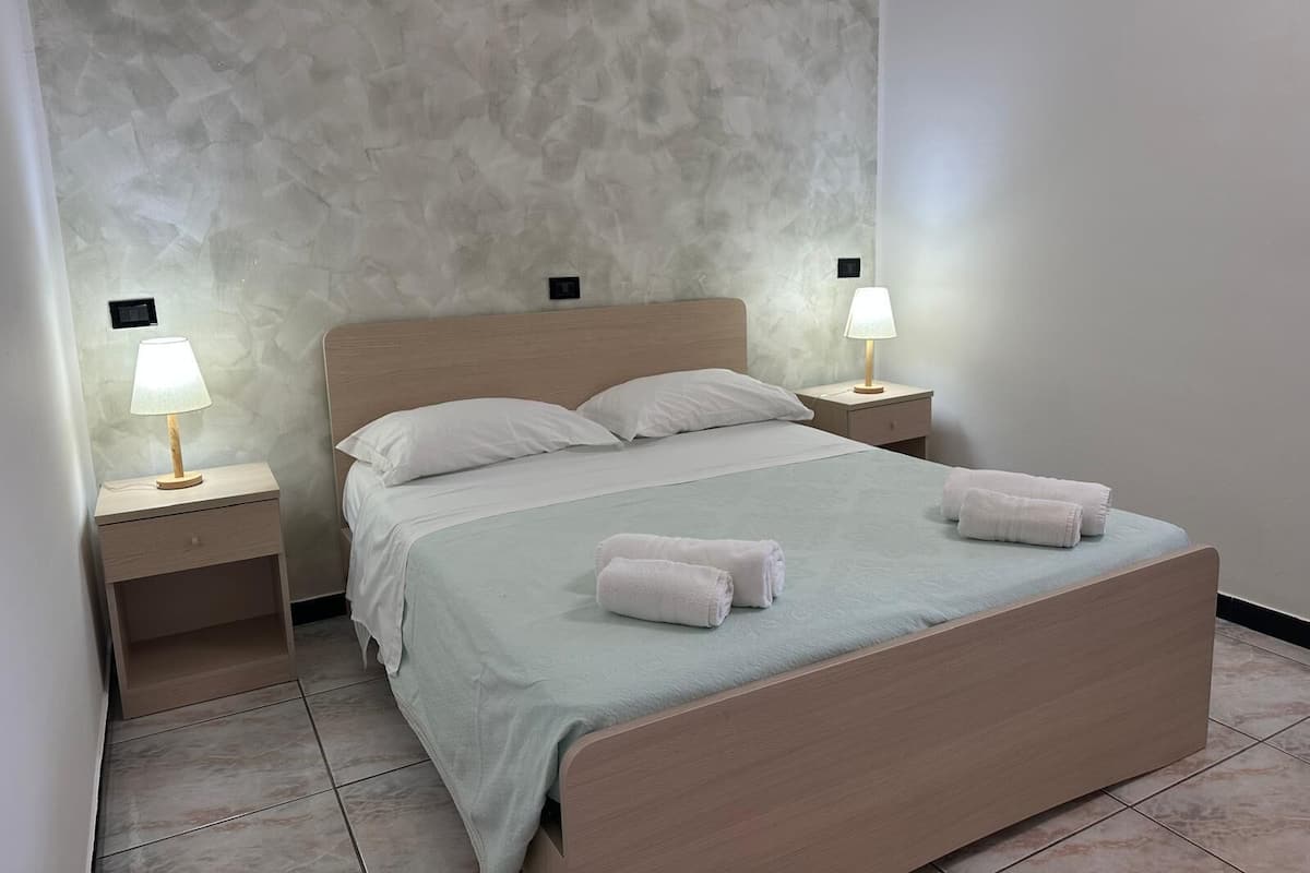 A neatly made bed with two pillows, two bedside lamps, and two rolled towels on the bed.