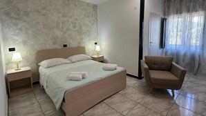 A bedroom with a bed, two bedside tables with lamps, a chair, and a door.