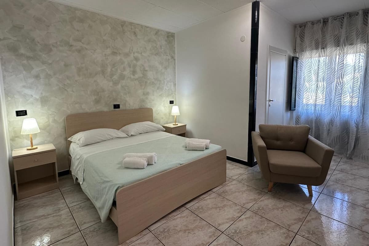 A bedroom with a bed, two bedside tables with lamps, a chair, and a door.