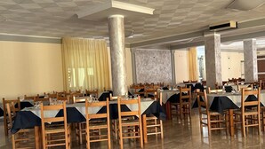 A spacious dining hall with multiple tables and chairs, large columns, and a checkered ceiling.
