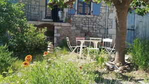 A stone building with blue shutters, a balcony, and a table with chairs in the foreground. - In the heart of the Ardeche river (Vogüé)