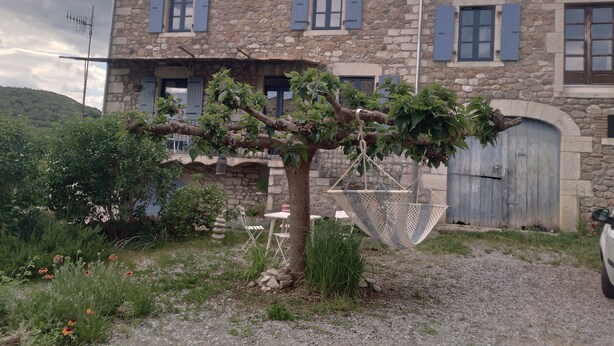 A stone building with a large tree in front, a gravel path, and a metal chair. - In the heart of the Ardeche river (Vogüé)