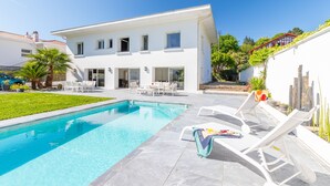 Une maison moderne à deux étages, dotée d’une piscine, d’un espace de détente extérieur et d’un jardin bien entretenu.