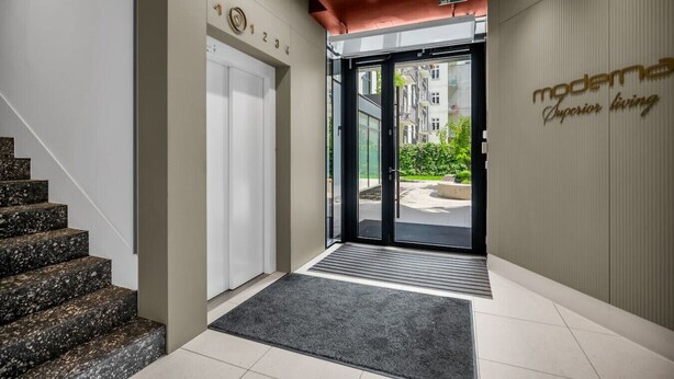 Entrada de hotel con una escalera, una puerta con números y un letrero que indica una zona superior.