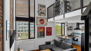 Un loft moderno con cama alta, comedor, cocina y sala de estar con sofá gris y una mesa de centro.