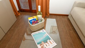 A magazine on a glass table, a basket with snacks, a bottle, and a bag of chips in a living room with a sofa and wooden flooring.