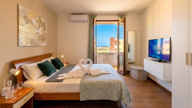 A hotel room with a bed, a TV, a balcony with a view, and an air conditioning unit.
