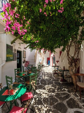 An outdoor café with stone flooring, green and red chairs, and pink flowers. - Mr & Mrs Mykonos The Residence (Mykonos)