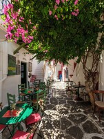 Un café en plein air avec un sol en pierre, des chaises vertes et rouges, et des fleurs roses.