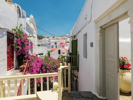 Uma rua estreita com edifícios brancos, uma porta vermelha e flores cor-de-rosa.