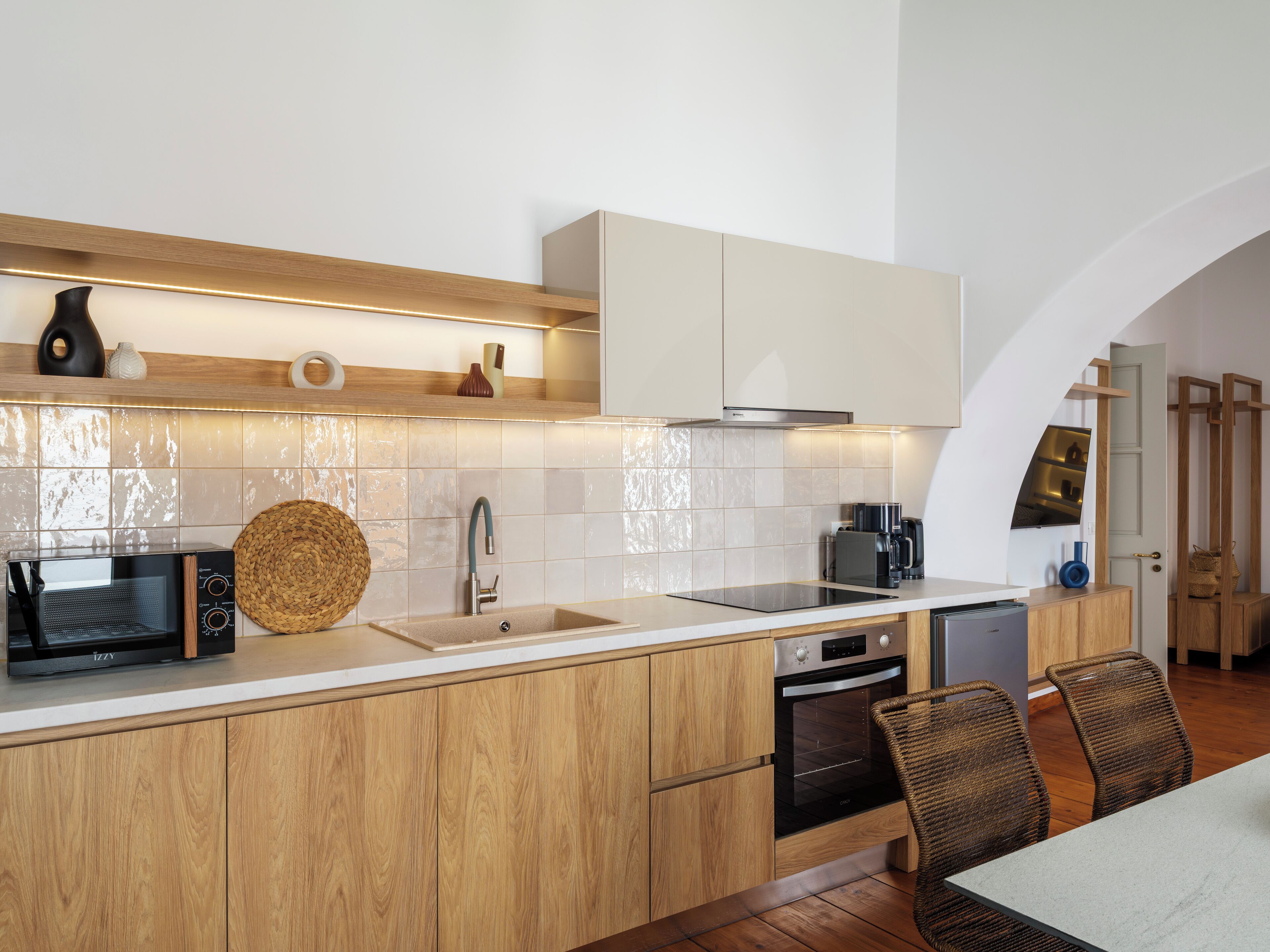 Una cocina moderna con armarios de madera, horno empotrado, microondas y cafetera.