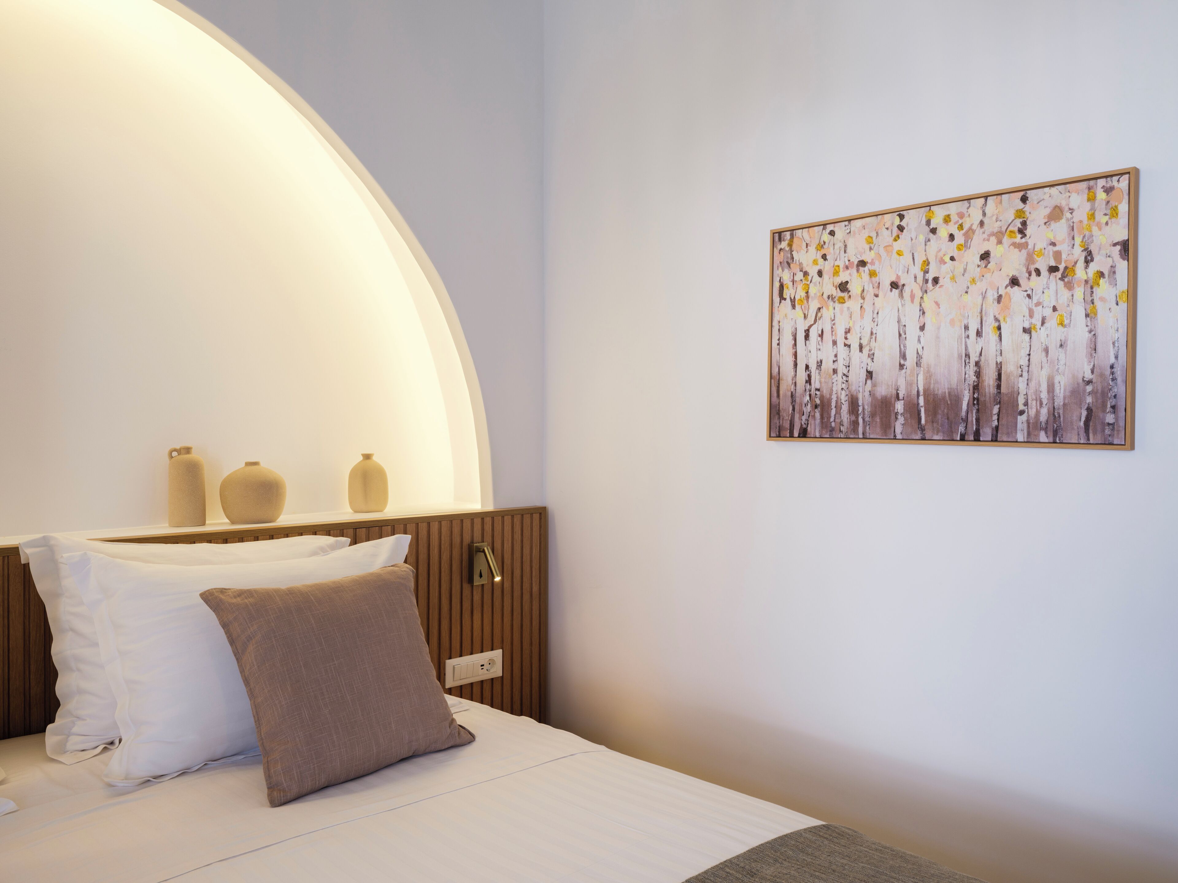 A bedroom with a bed, a bedside table with two vases, a wall-mounted painting, and a curved ceiling light.