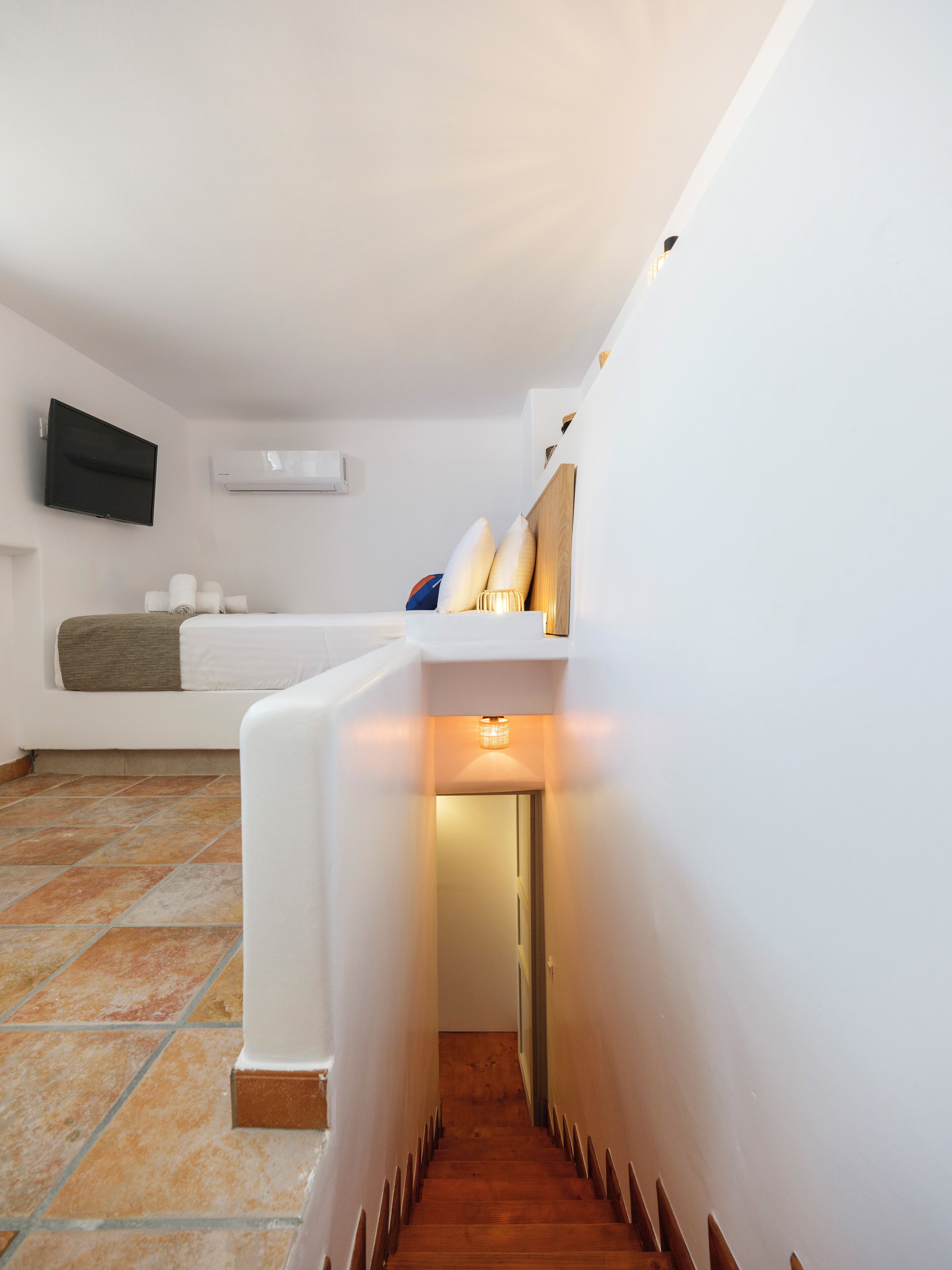 Habitació d'hotel moderna amb llit blanc, televisió de pantalla plana, aire condicionat i terra de rajola.