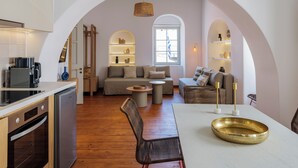 Una cocina moderna con horno integrado y cafetera, un comedor con mesa redonda y sillas, y una sala de estar con sofá y mesa baja.