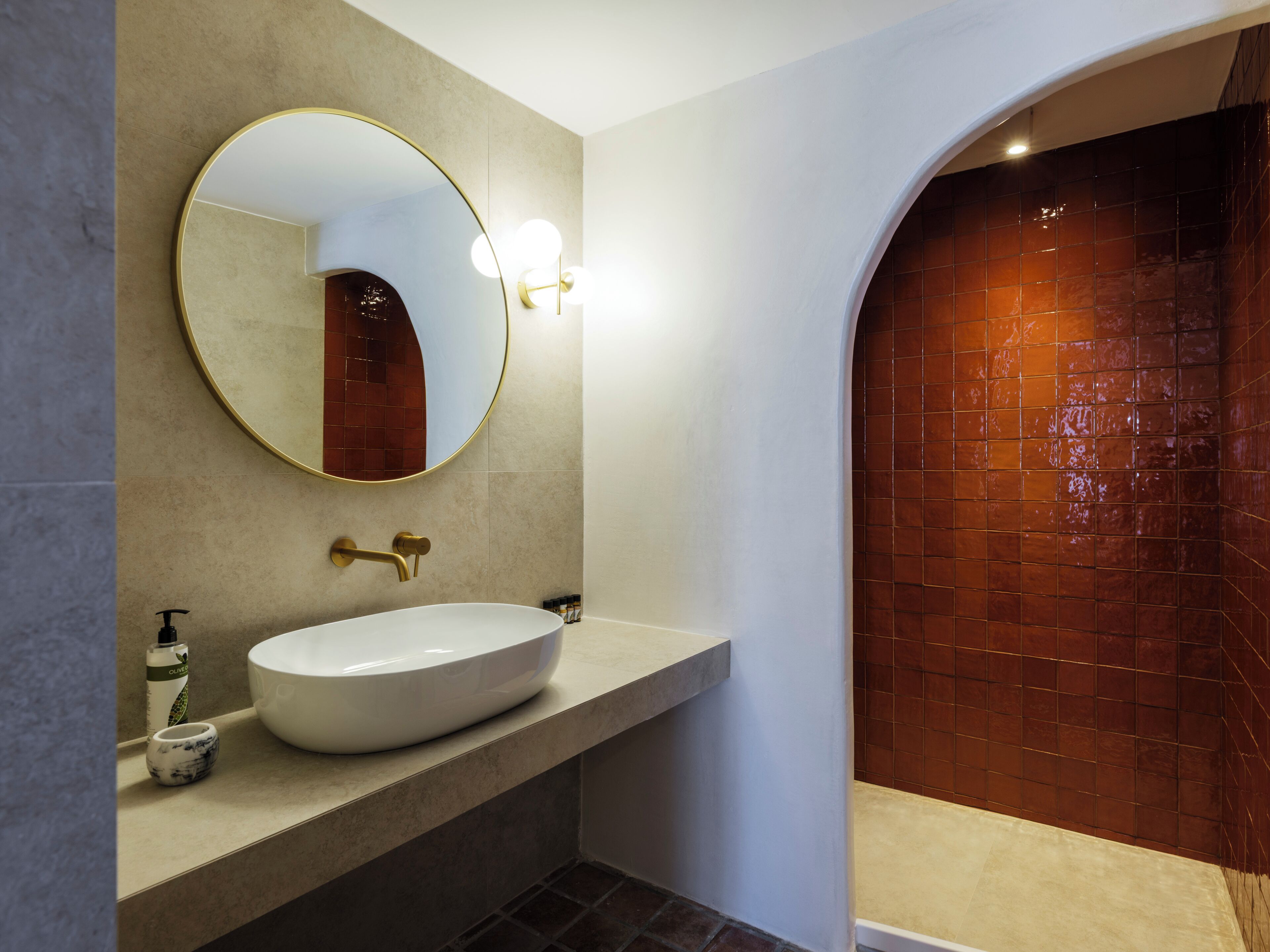 A bathroom with a round mirror, a white sink, and a tiled shower area.