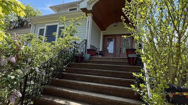 A two-story house with a front porch, a staircase leading to the entrance, and a clear blue sky.