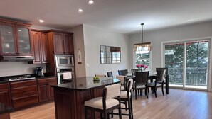 A modern kitchen with wooden cabinets, a central island, and a dining area with chairs and a table.