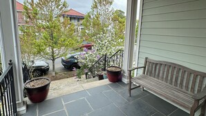 A covered porch with a wooden bench, potted plants, and a view of a residential street.