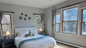 A bedroom with a bed, nightstands, a window with curtains, and a view of trees.