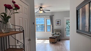 A hallway with a wooden bench, a vase with flowers, a ceiling fan, and a chair with a floral cushion.