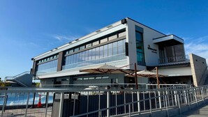 Un edificio moderno con fachada de vidrio, una zona de estar al aire libre techada y un letrero con el nombre visible.