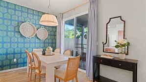 Un comedor con mesa blanca, sillas de madera, una consola negra con espejo y pared de diseño azulado.