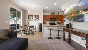 A modern kitchen with wooden cabinets, a dining area with a table and chairs, and a large painting on the wall. - Relaxed Island Living- WD, AC, Backyard, Workspace (Ewa Beach)